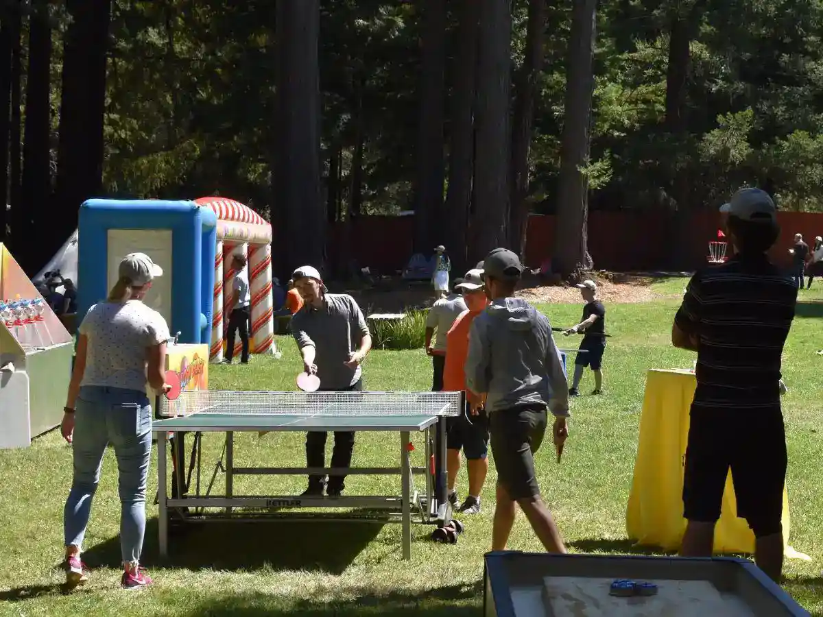 People playing table tennis at an outdoor event on a grassy lawn