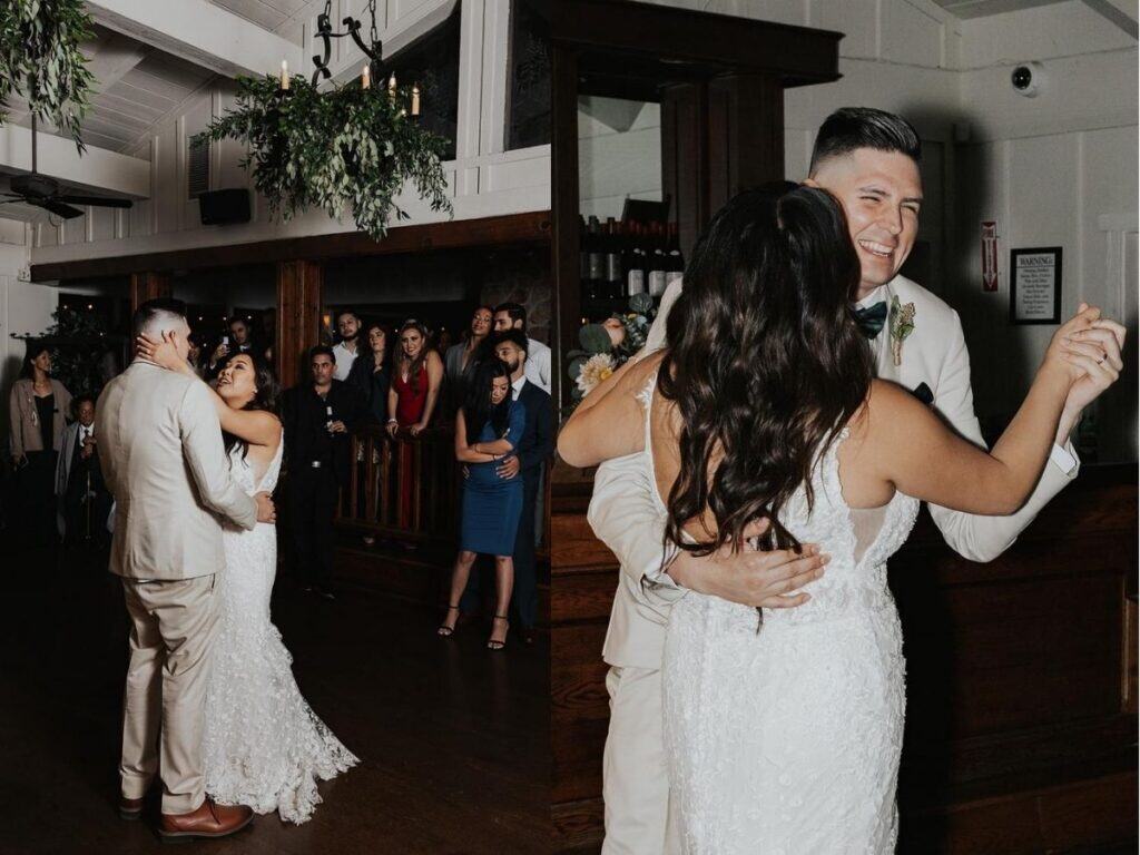 Bride and groom sharing their romantic first dance at a wedding reception, surrounded by guests. The bride wears a lace gown, and the groom is in a beige suit. The atmosphere is joyful and intimate.