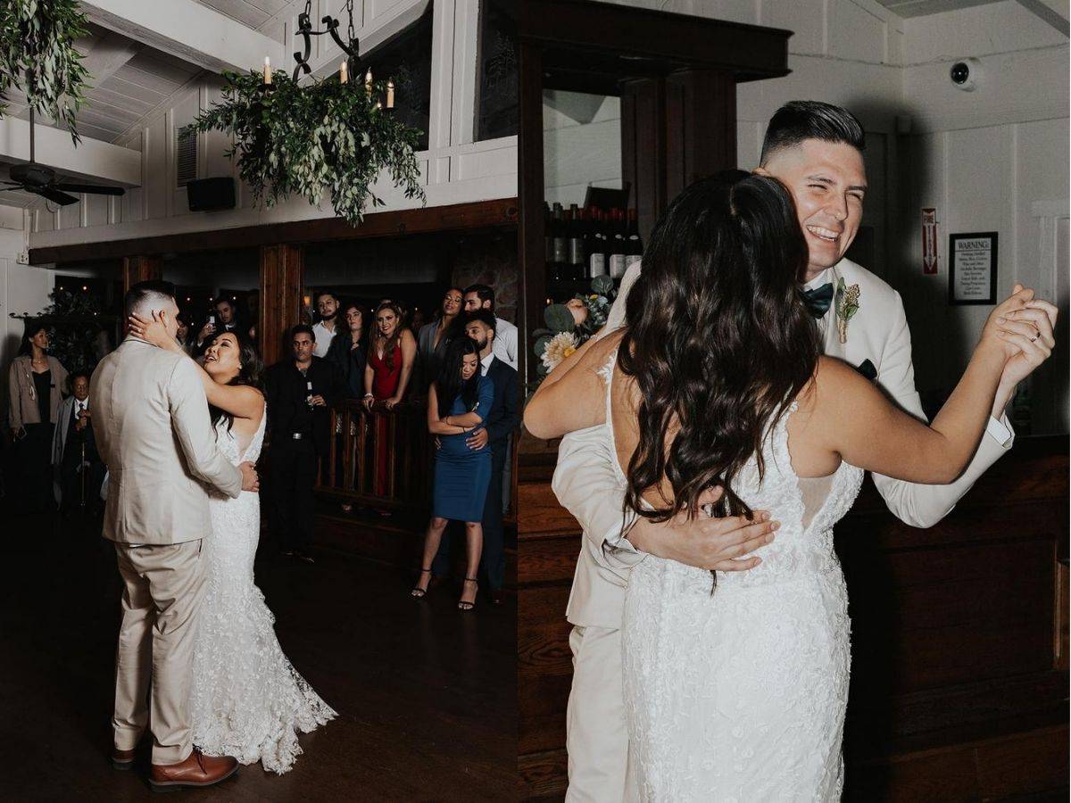 Bride and groom sharing their romantic first dance at a wedding reception, surrounded by guests. The bride wears a lace gown, and the groom is in a beige suit. The atmosphere is joyful and intimate.