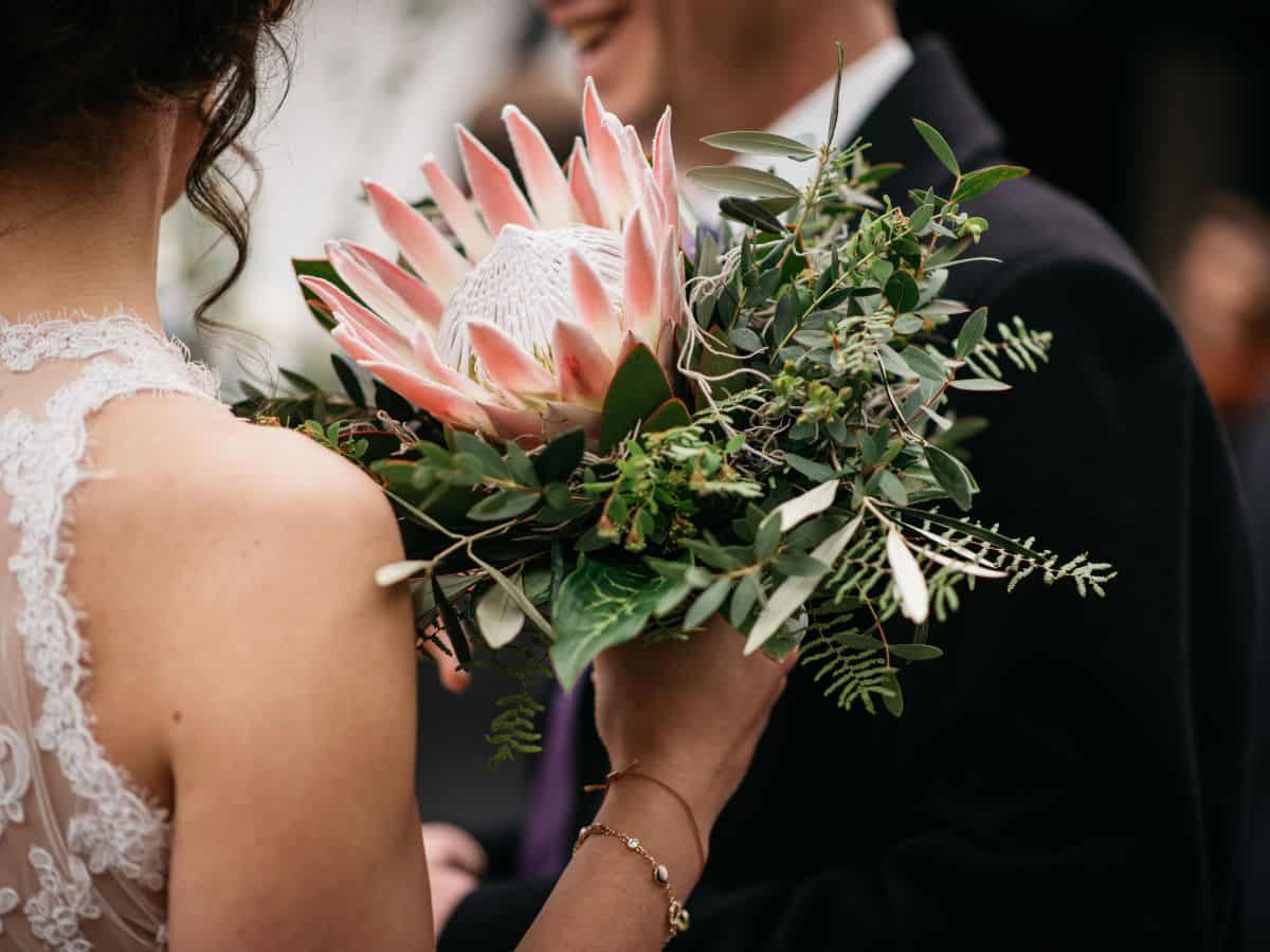 Wedding bride holding blush pink protea flower bouquet with groom