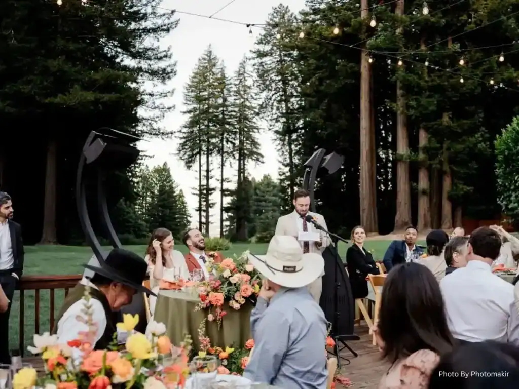 Wedding guest gives a speech outdoors as guests listen beneath string lights