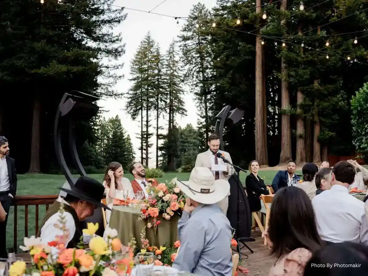 Wedding guest gives a speech outdoors as guests listen beneath string lights