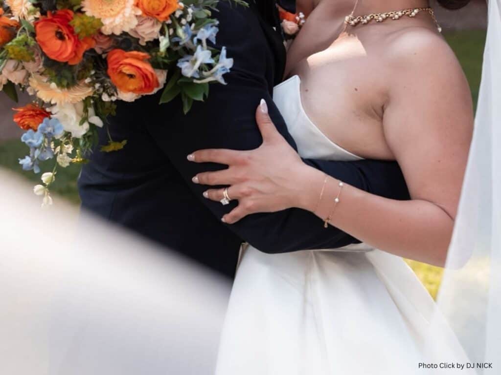 Bride and groom embracing, showing the bride’s hand with wedding rings and a colorful bouquet