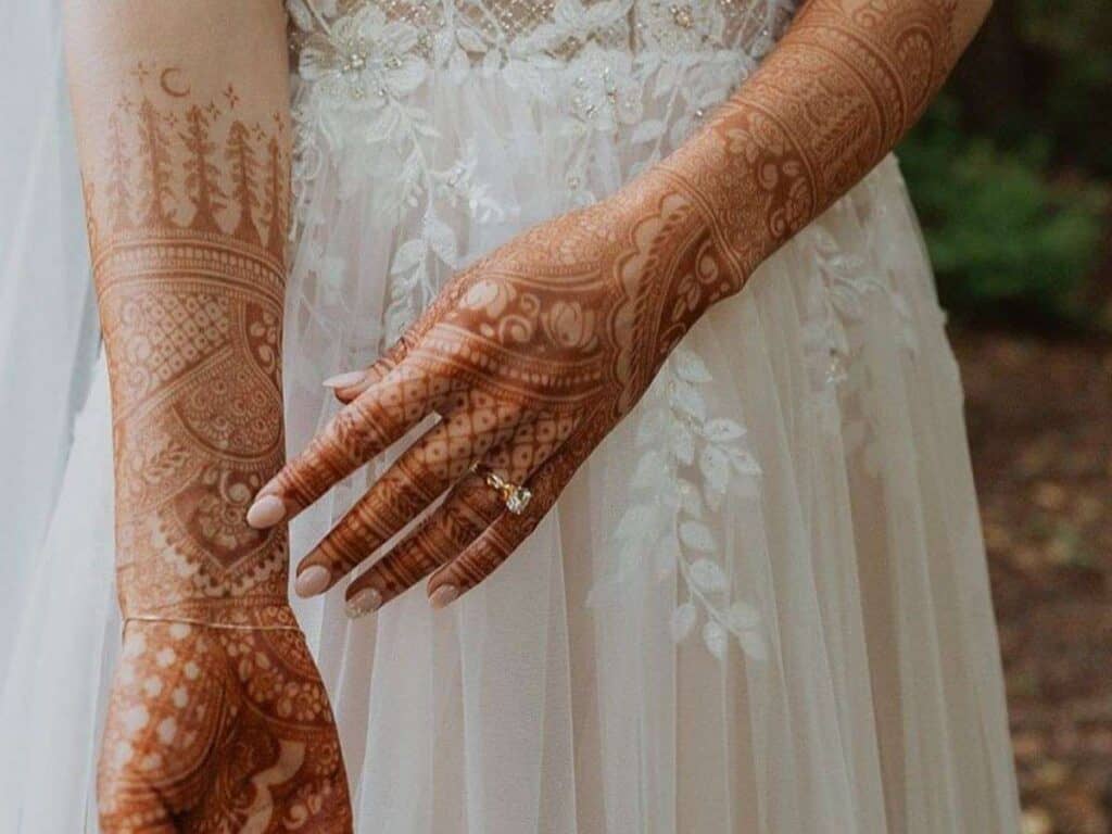 Bride’s hands with detailed henna and a wedding ring on a white dress background