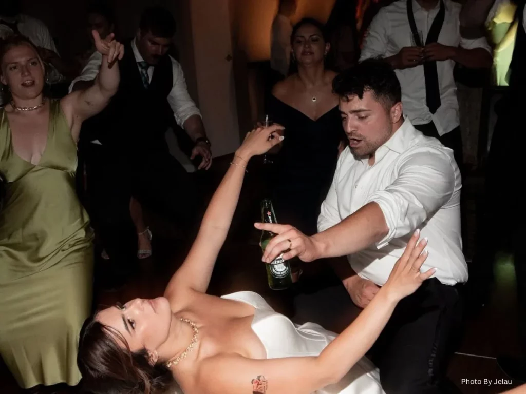 A bride and groom dancing energetically at a wedding reception with guests celebrating around them