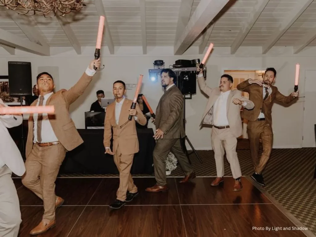 A group of groomsmen in suits dancing and celebrating at a wedding reception with glow sticks in hand
